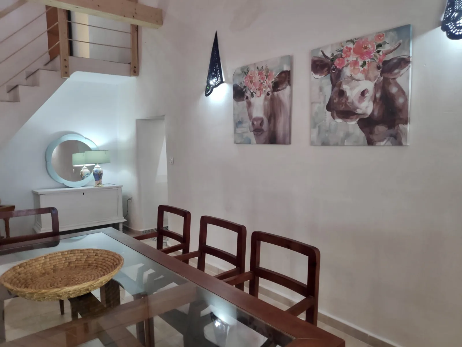 Comedor con mesa de cristal, sillas de madera y escalera al altillo